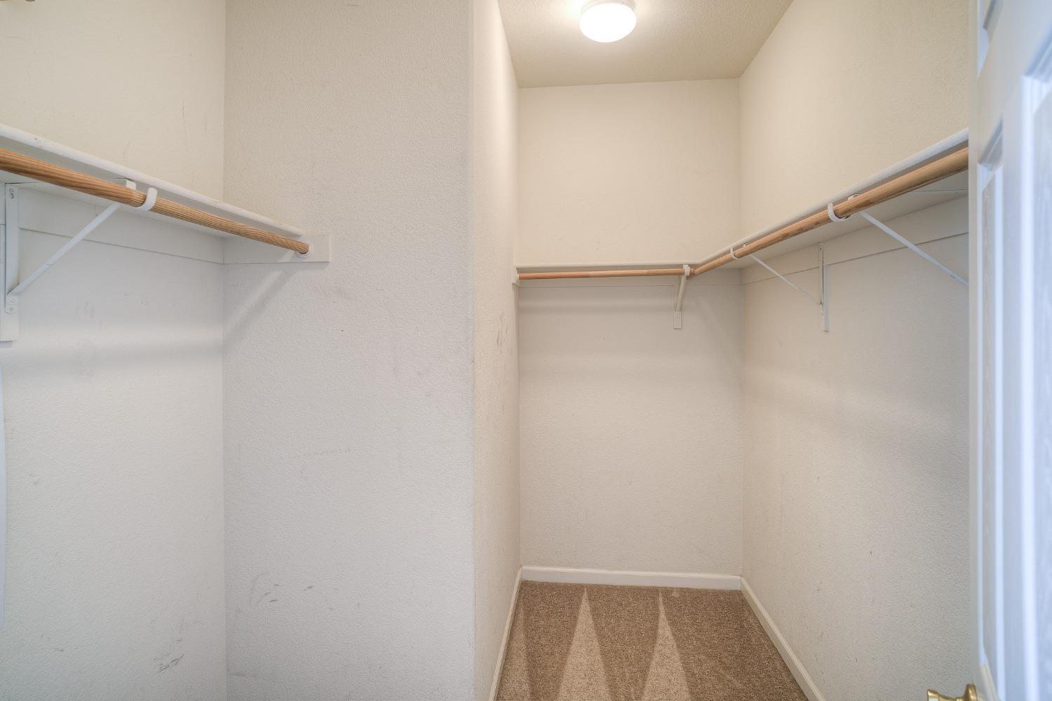 Empty walk-in closet with carpeted floor and wooden hanging rods along three walls.