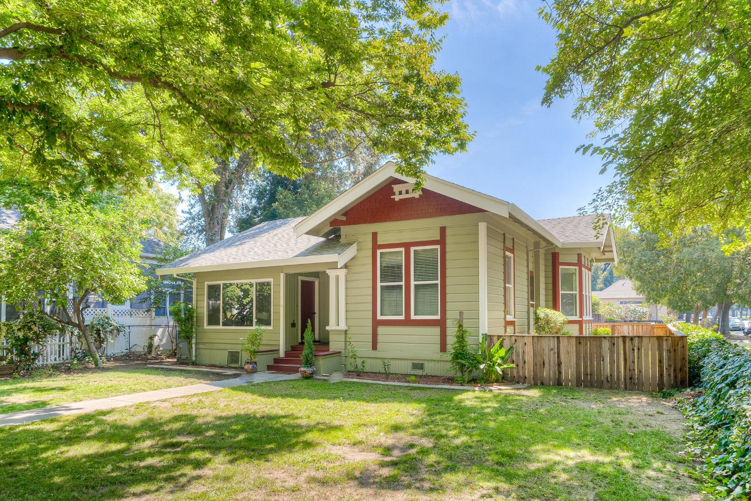 Sage-green Craftsman house with red trim, shaded by mature trees and fronted by a lawn.