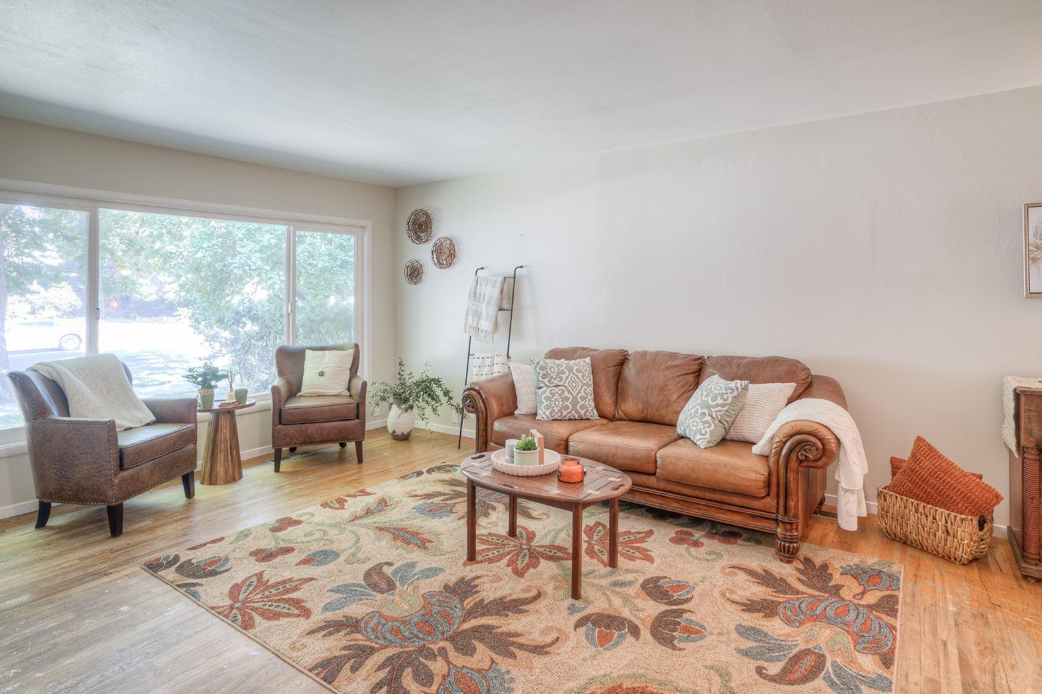 Staged living room with brown leather seating, a large bright window, and a colorful floral rug.
