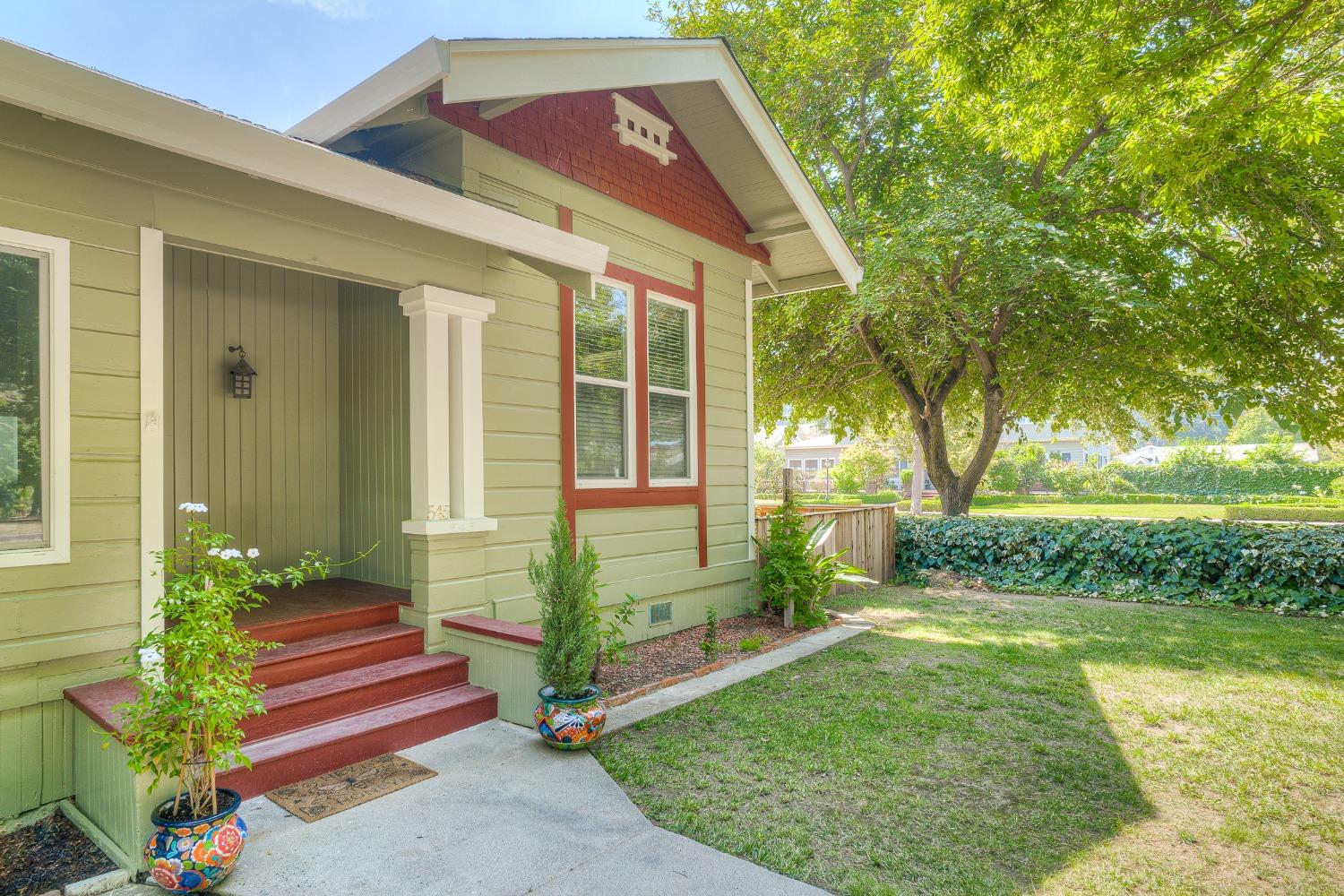 Pale green house with red trim, a covered porch, red steps, and a leafy yard.