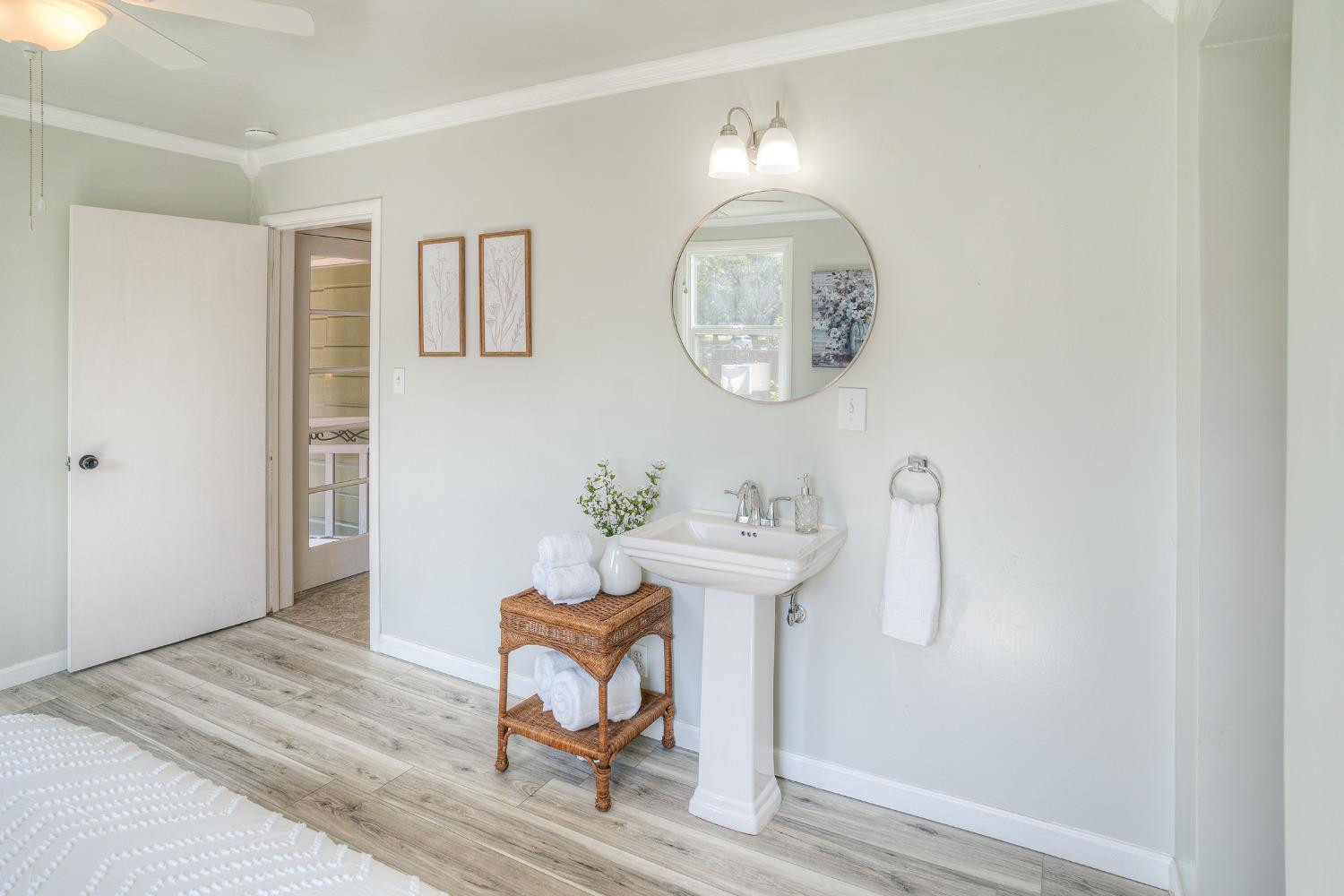 Bright bathroom with a pedestal sink, round mirror, and wicker towel stand.