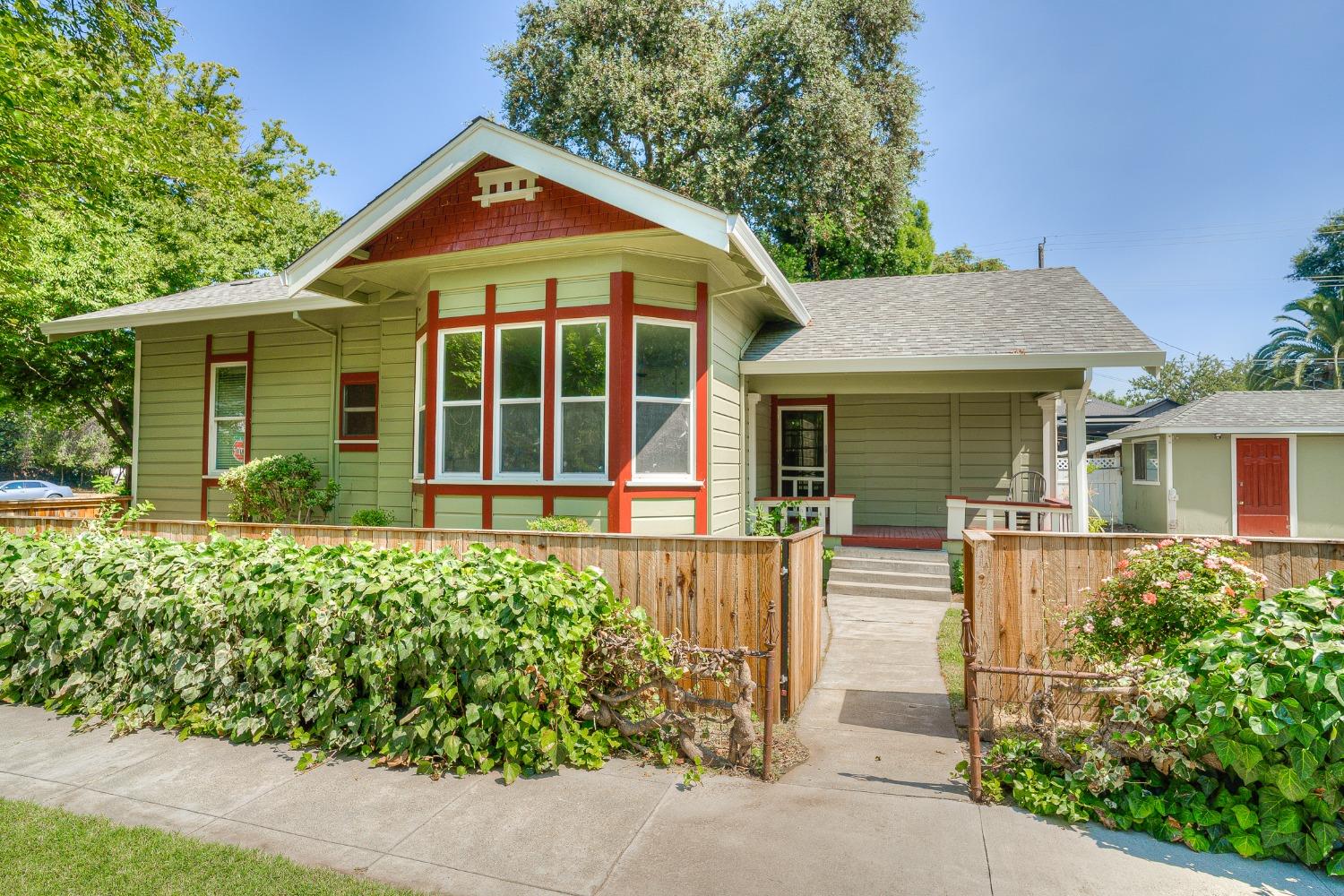 Green Craftsman-style house with red trim, covered porch, and fenced walkway to the entrance.