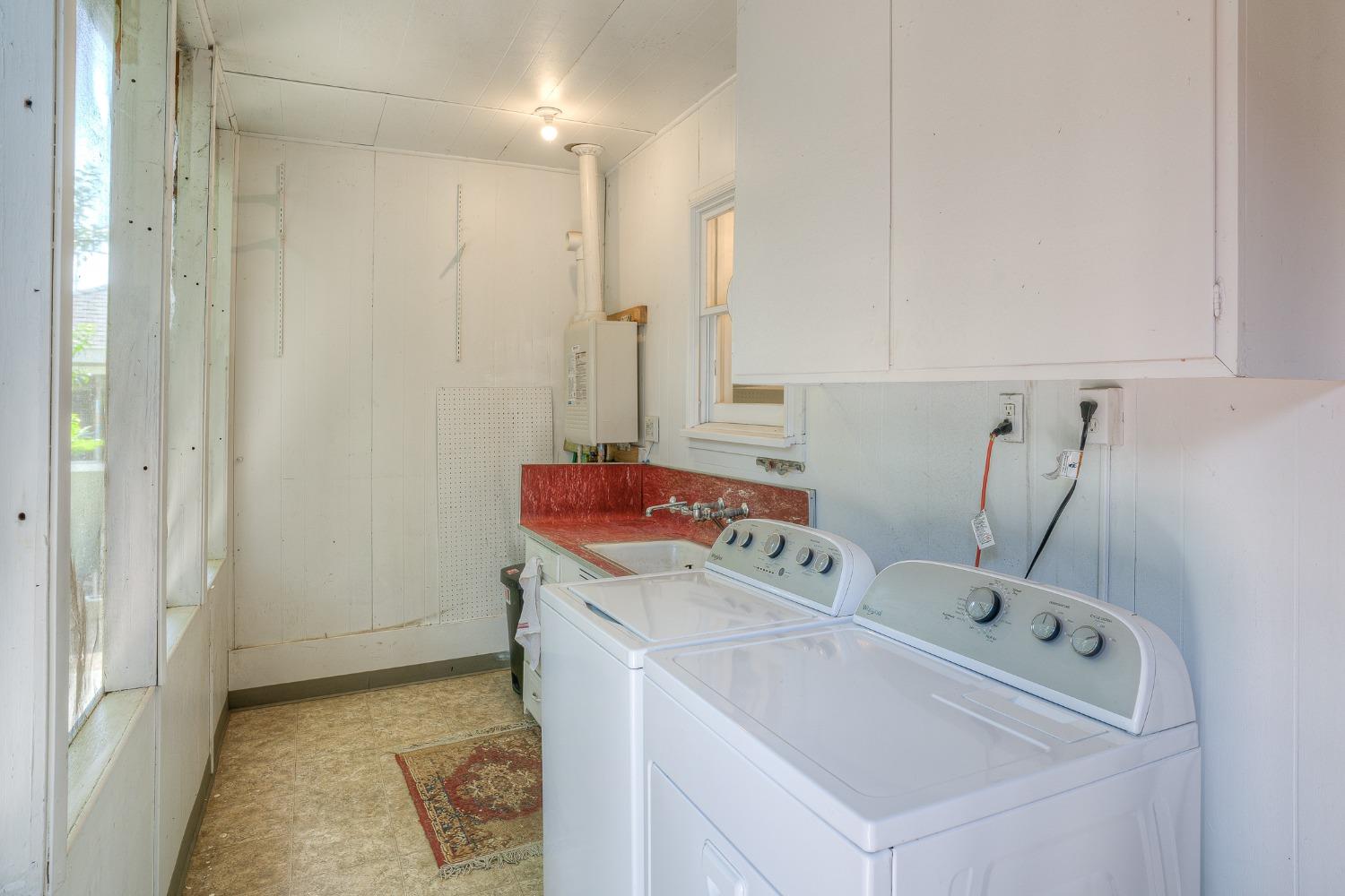 Laundry room with a top-loading washer and dryer beside a utility sink and window.