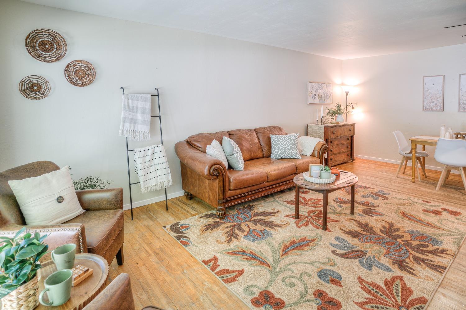 Living room with a brown leather sofa, colorful patterned rug, and adjoining dining area.