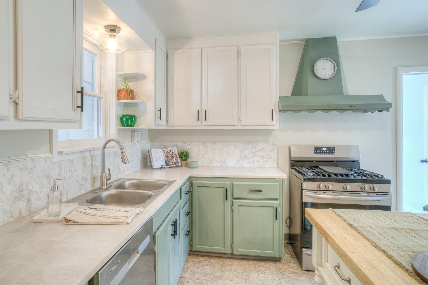 Kitchen with pale green cabinets, marble-pattern backsplash, stainless steel range, and double-basin sink.