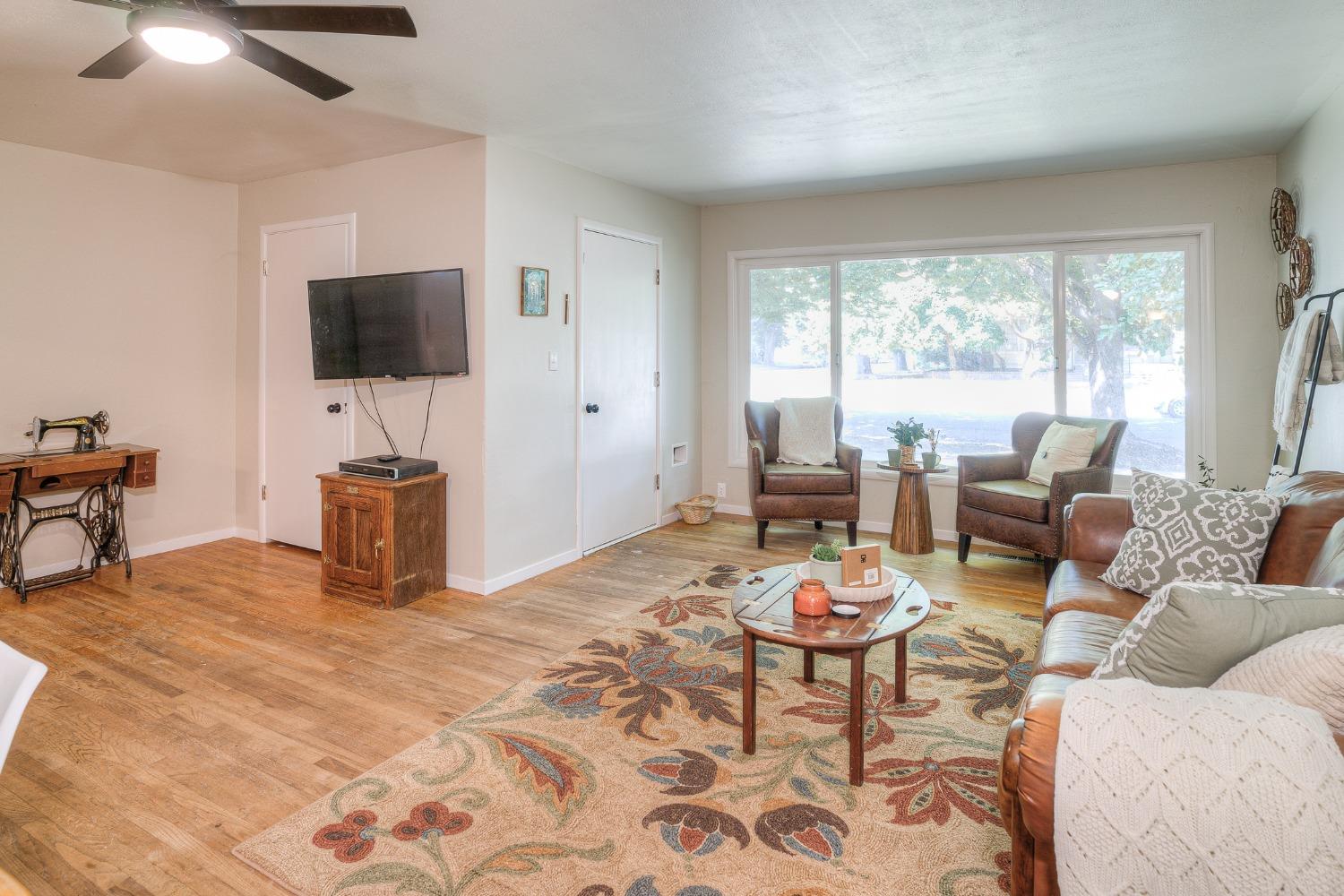 Living room with leather seating, hardwood floors, and a wide window overlooking trees.