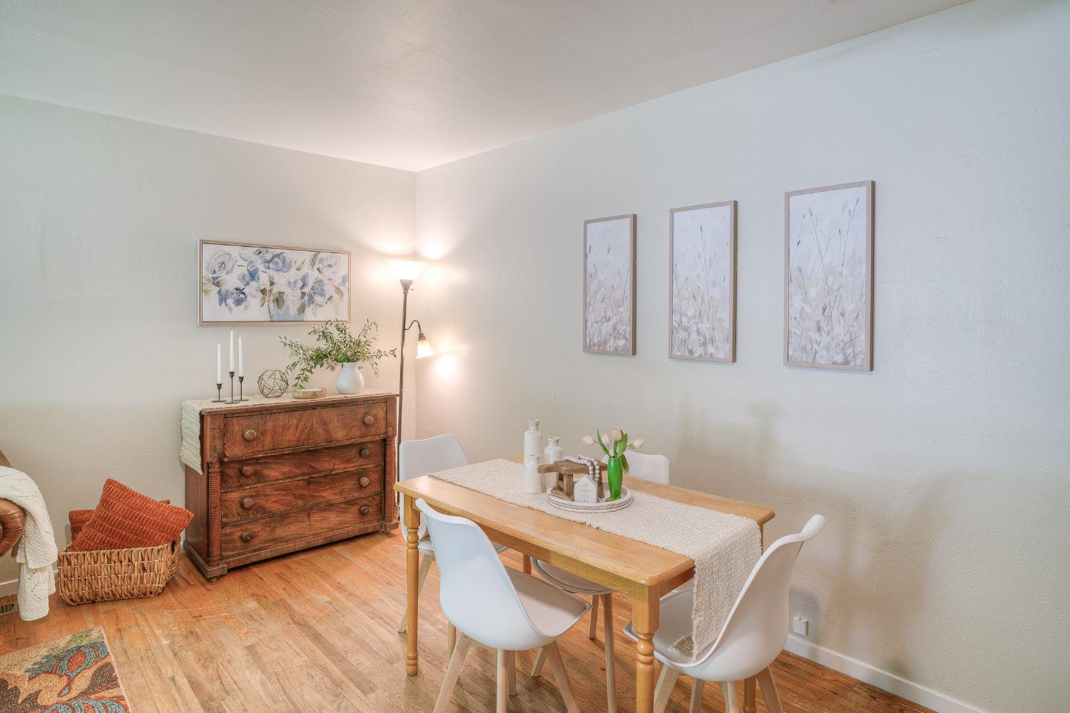 Dining room with a wooden table, white chairs, hardwood floors, and a vintage chest of drawers.