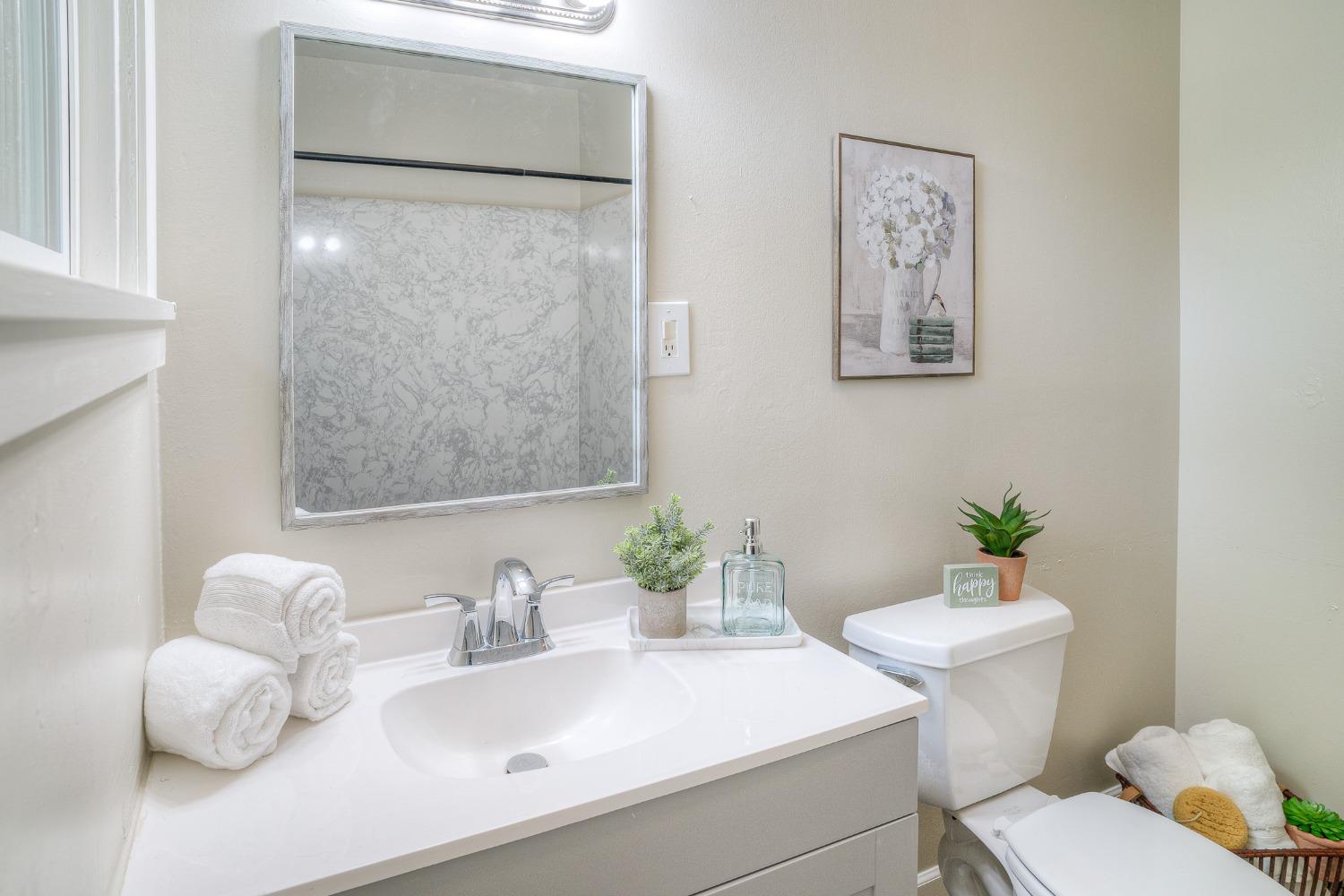 Bathroom with a white vanity, large mirror, and marble-patterned shower surround.