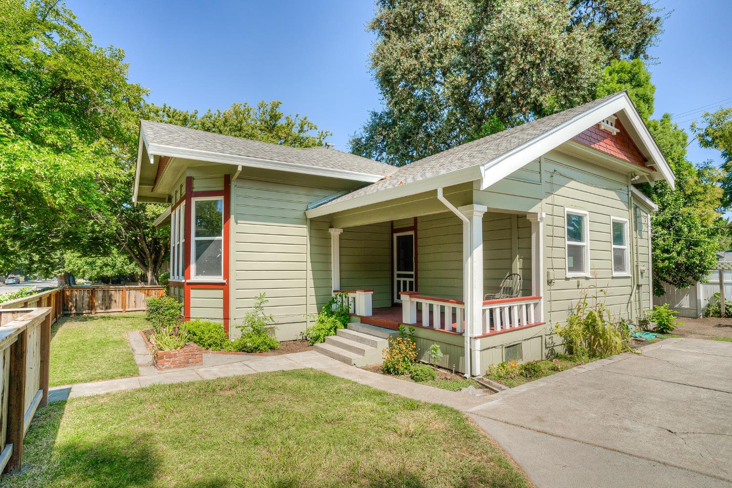 Pale green bungalow with red trim and a covered porch, surrounded by trees and a small lawn.