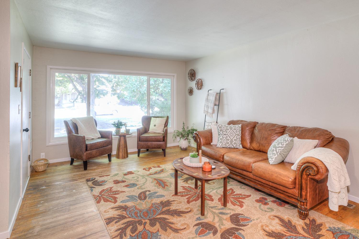 Living room with a brown leather sofa, two armchairs, and a large floral rug beside a wide window.