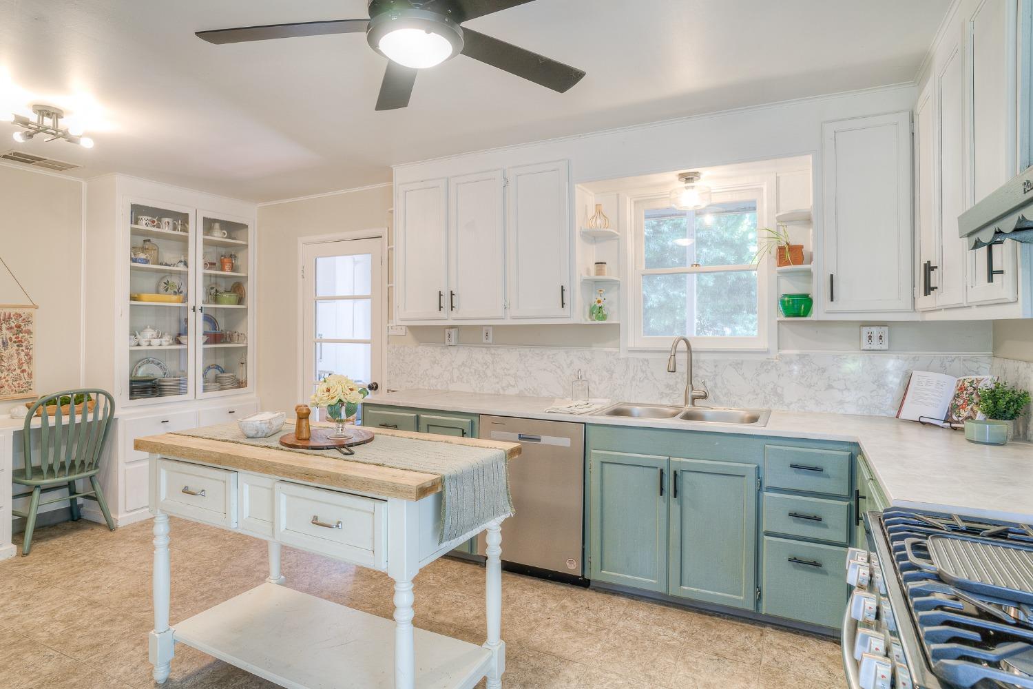 Kitchen with blue-green lower cabinets, a central island, and a sink beneath a window.