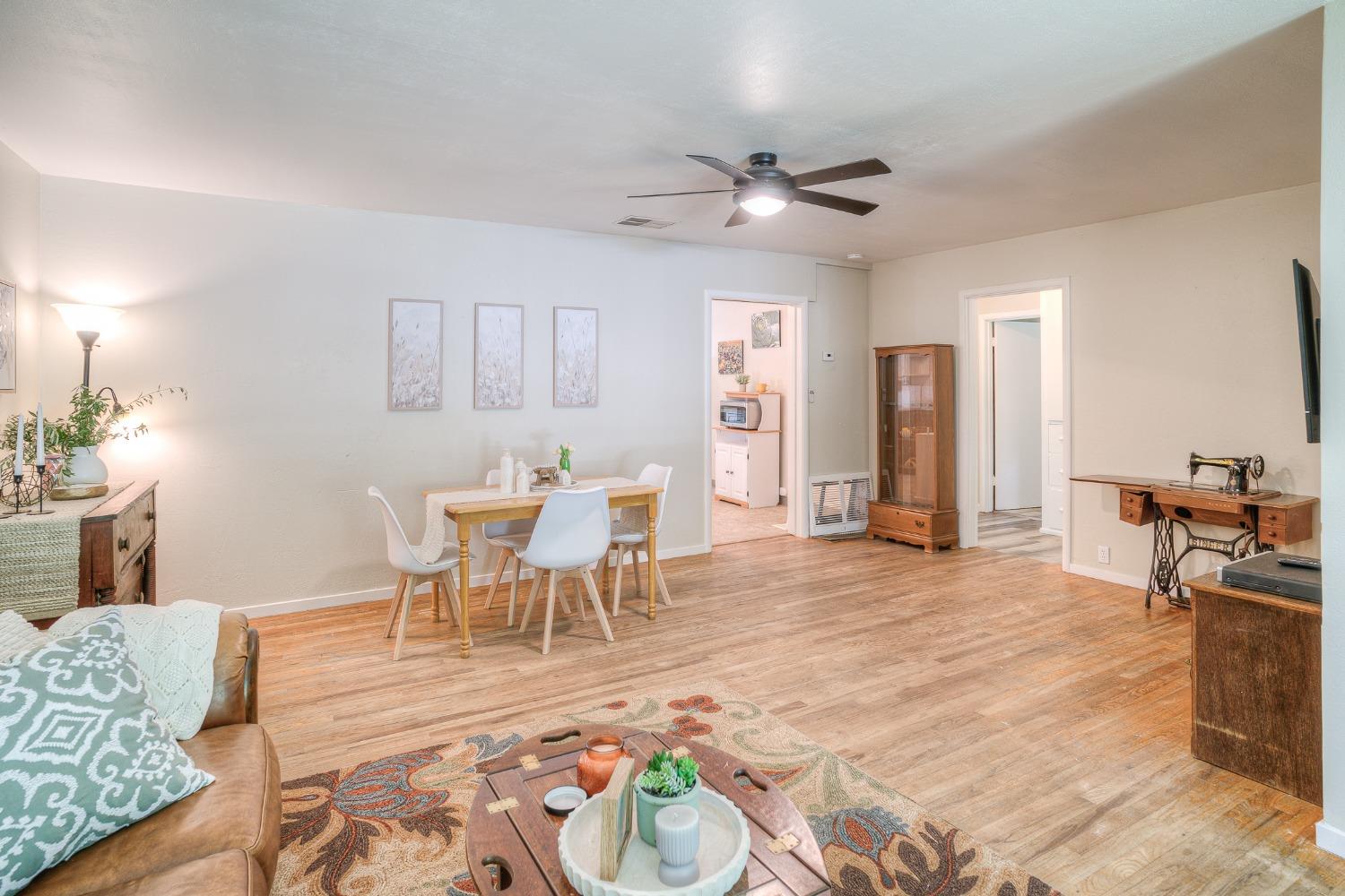 Furnished living and dining room with light wood floors, a ceiling fan, and a sewing machine on a desk.