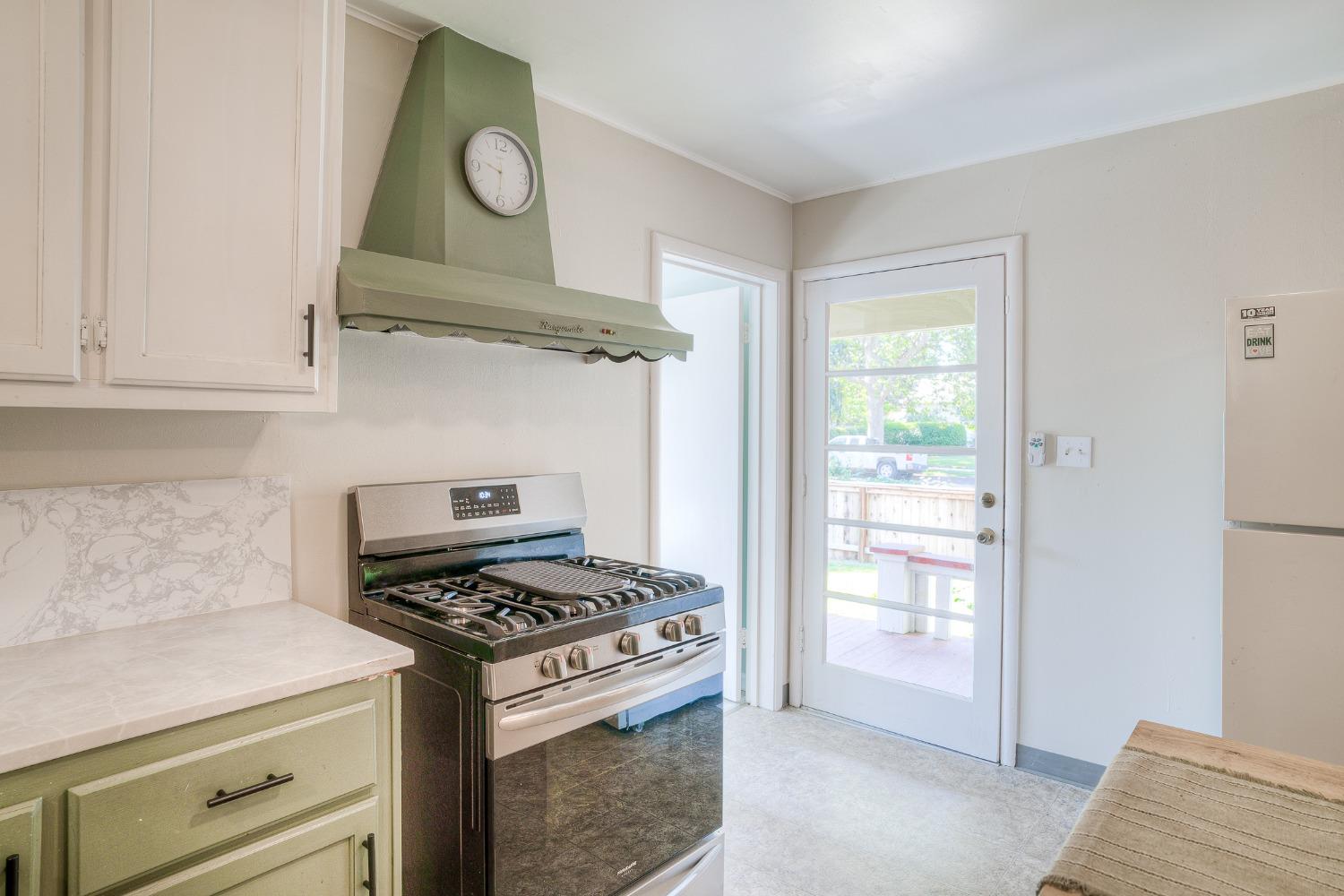 Kitchen with pale green cabinets, stainless steel gas range, and a glass-panel door to the deck.