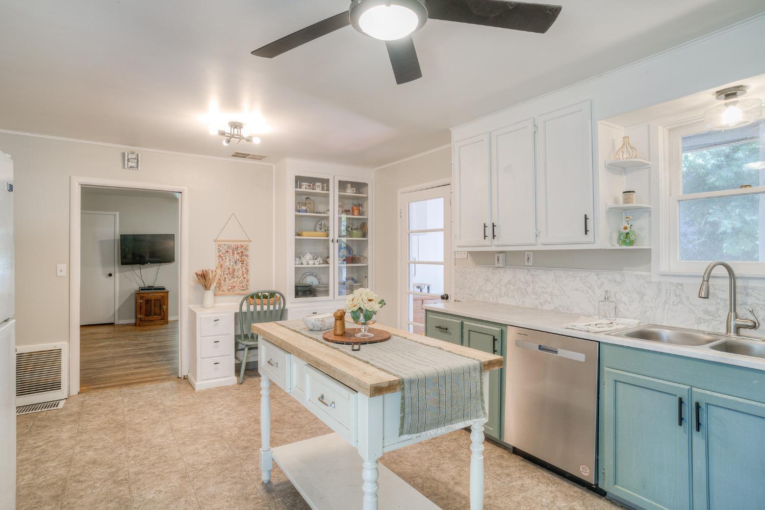 Kitchen with a wood-topped island, teal cabinetry, and white cabinets with glass-front display shelves.