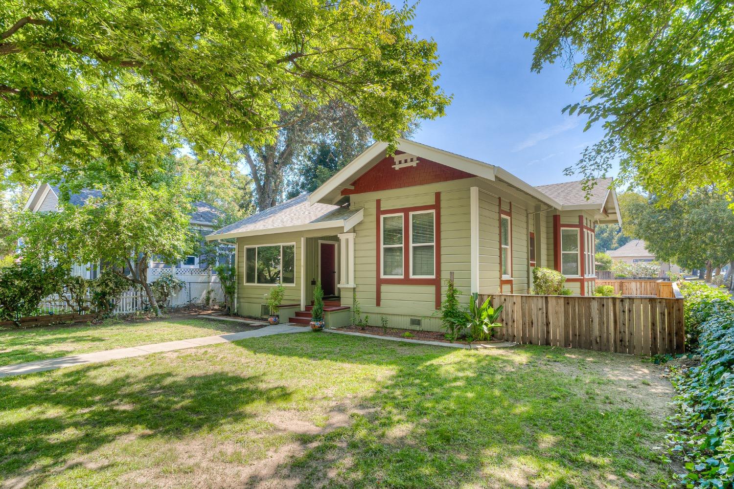 Single-story pale green house with red trim, a small porch, and a leafy front yard.