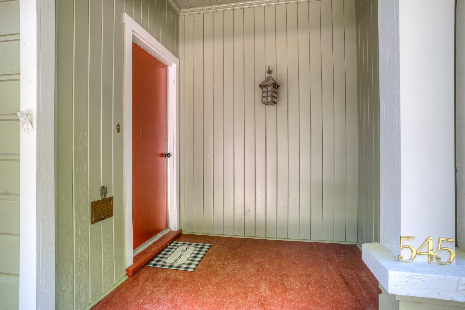 Front entry with a red door, paneled walls, porch lantern, and gold 545 house numbers.