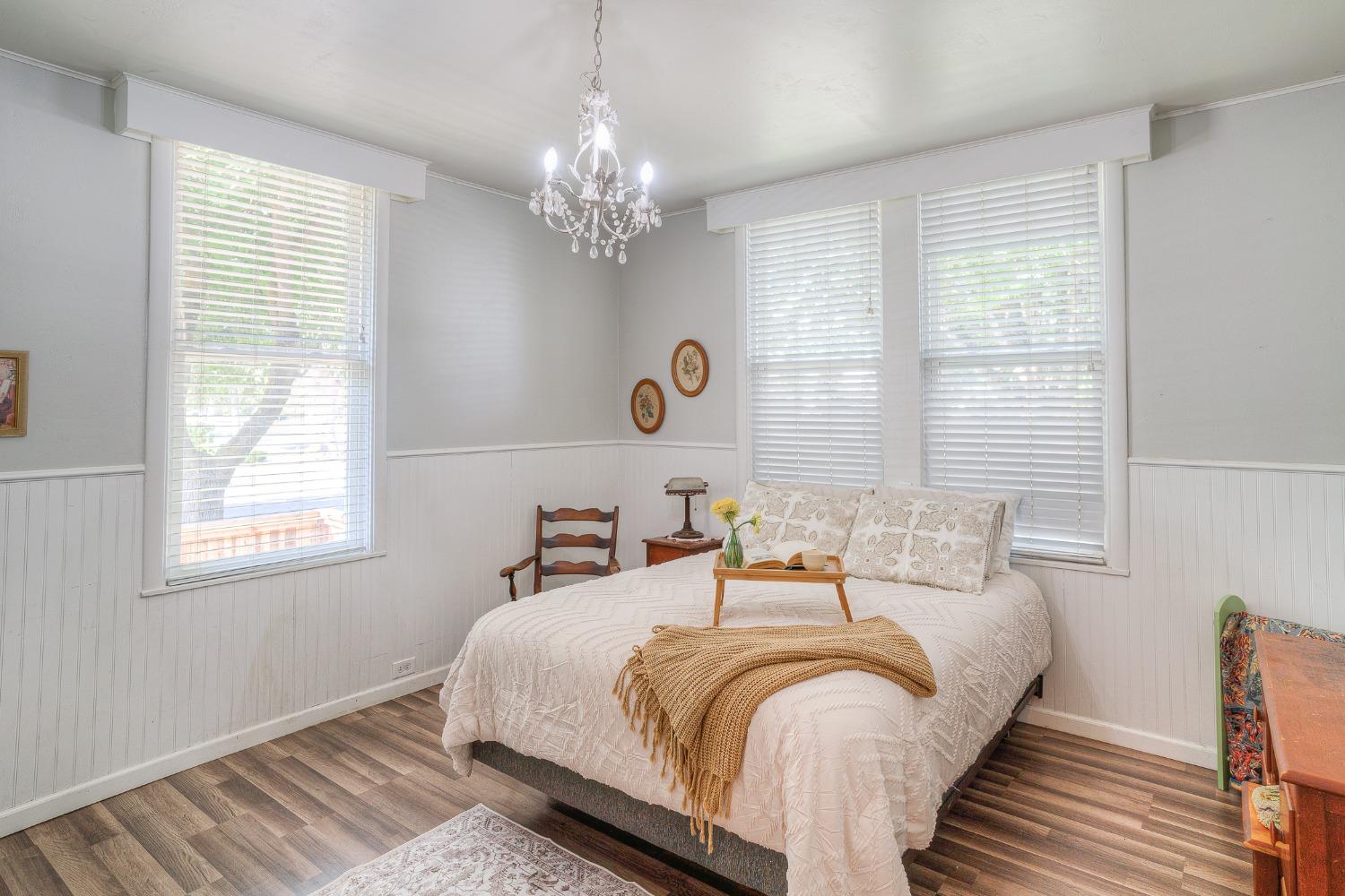 Bedroom with a white bed, three blind-covered windows, and a crystal chandelier.