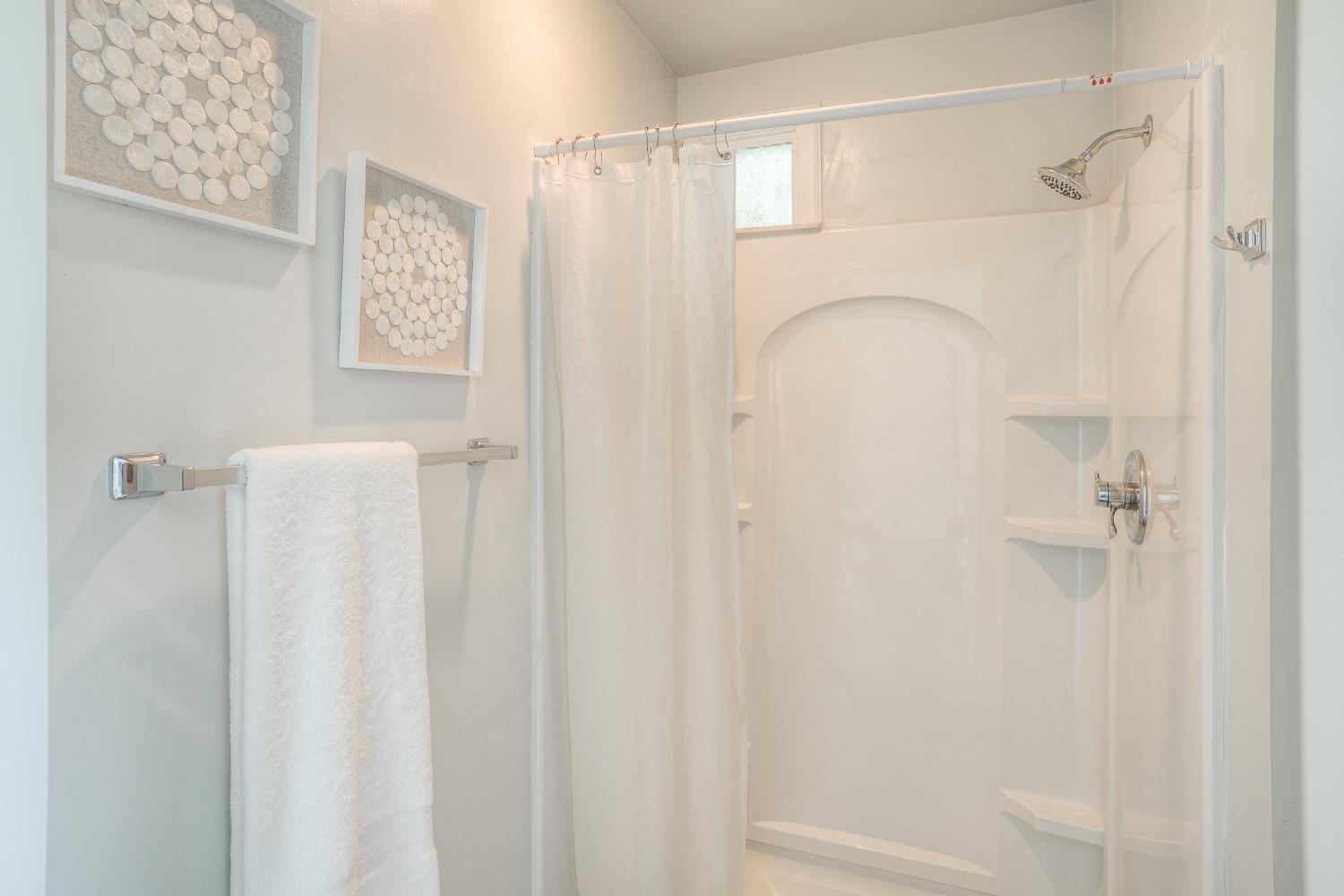 Bathroom shower and tub with built-in shelves, a white curtain, and framed wall art.