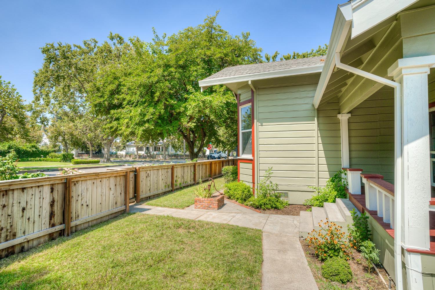House exterior with a covered porch, fenced yard, walkway, and leafy garden.