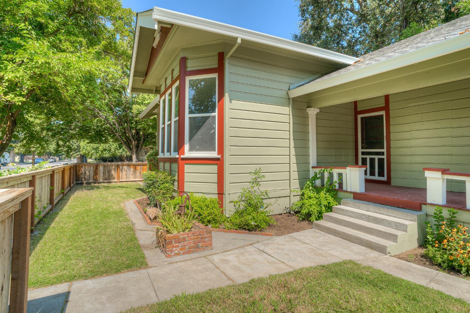 House exterior with red trim, covered porch, concrete steps, and fenced grassy yard.