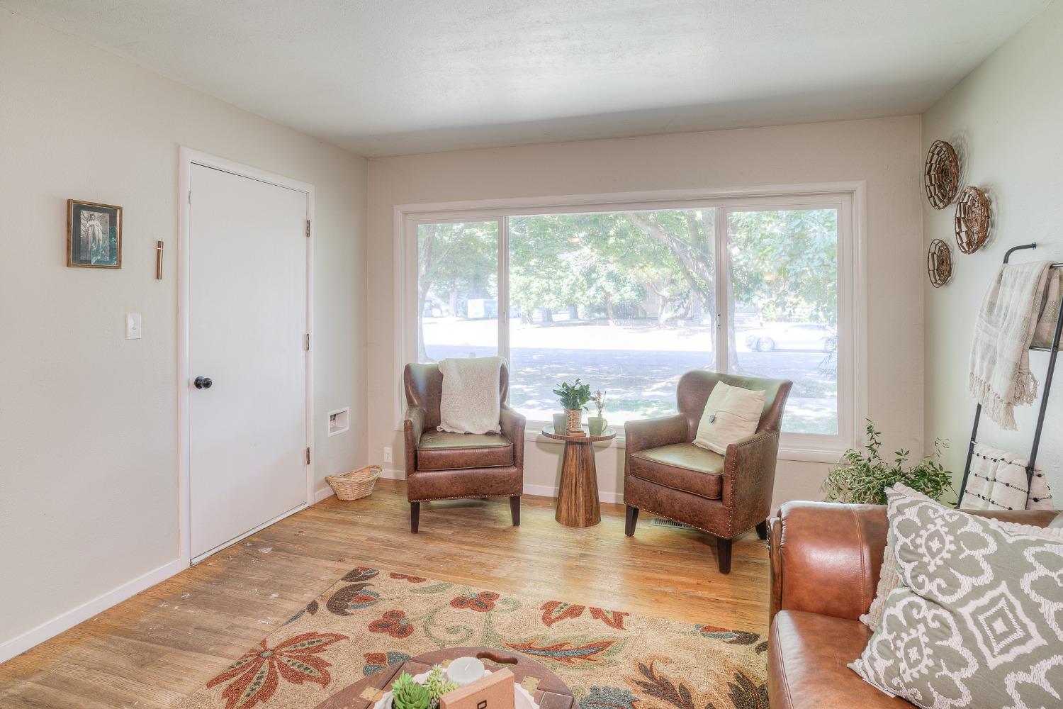Living room with leather armchairs, wood floors, and a wide window overlooking leafy trees.