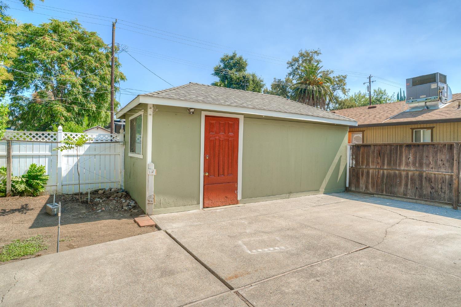 Green outbuilding with a red door beside a broad concrete driveway.