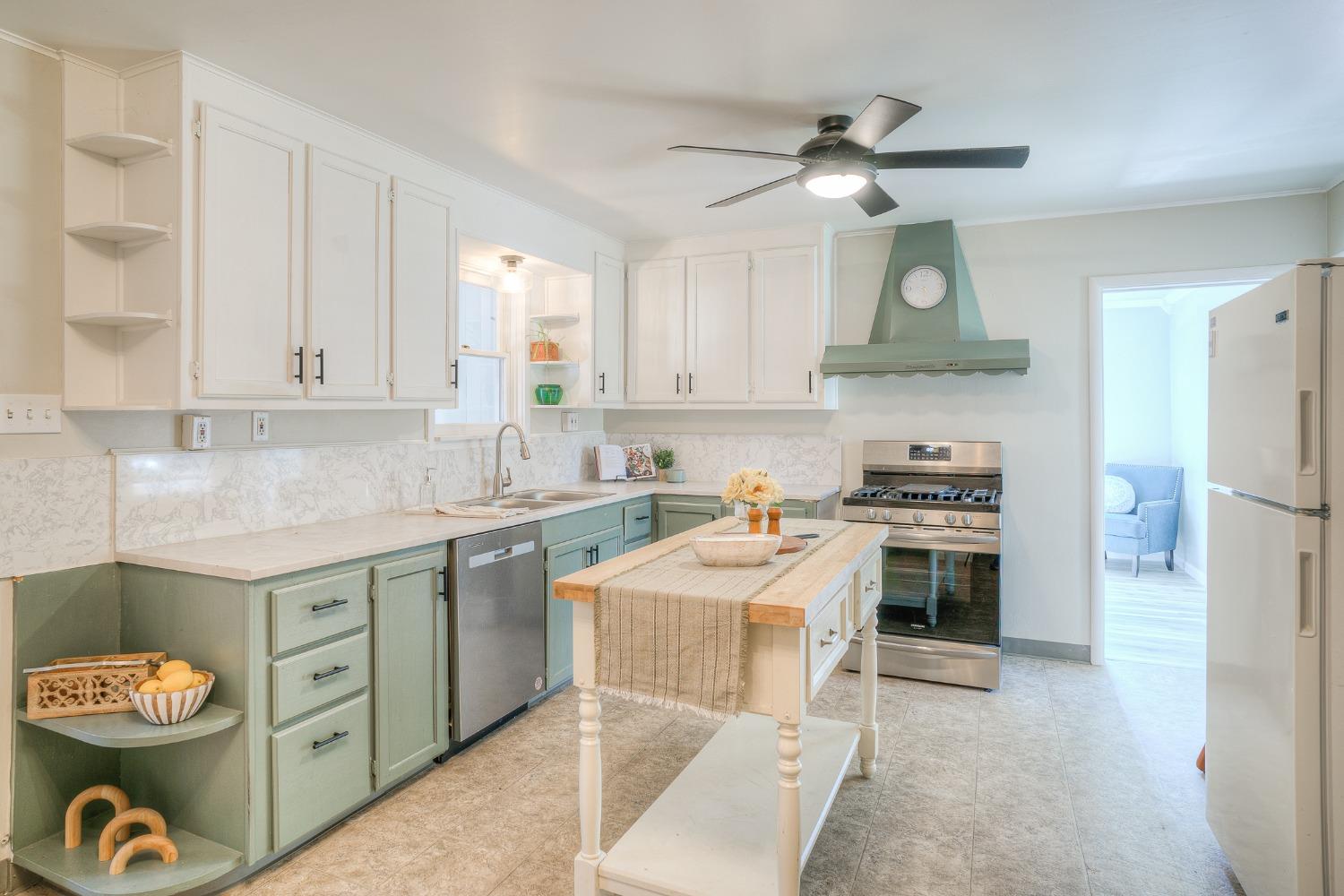 Kitchen with pale green cabinets, a central island, stainless steel appliances, and a sage green range hood.
