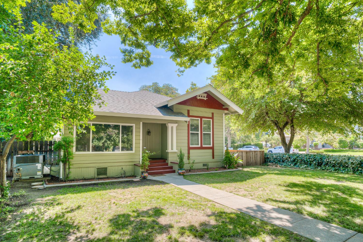Pale green house with red trim, a covered porch, and a shaded front lawn.