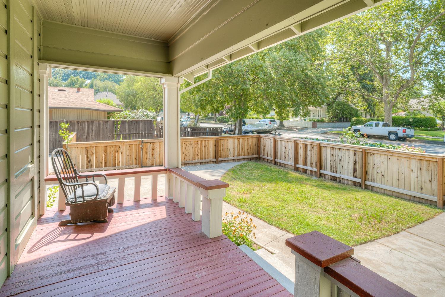 Covered porch with a rocking chair overlooking a fenced lawn and leafy residential street.