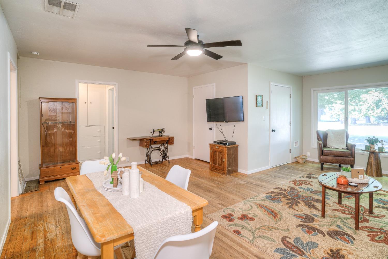 Combined living and dining room with wood floors, a patterned rug, and a large window.