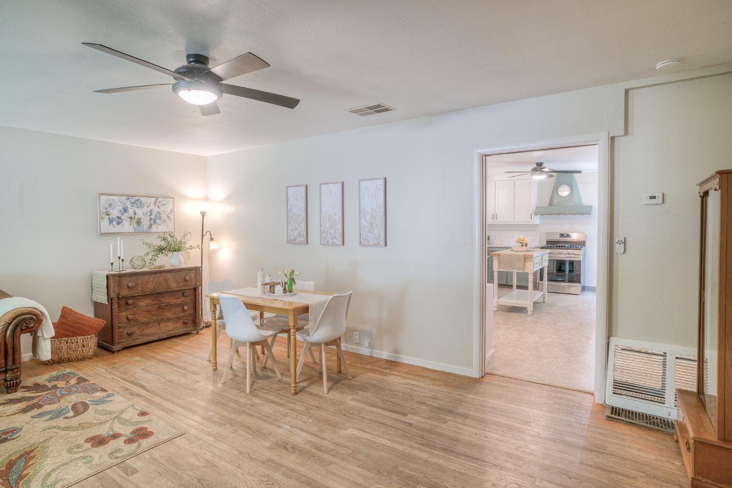 Dining room with a wooden table and white chairs, opening onto a kitchen with a stainless steel range.