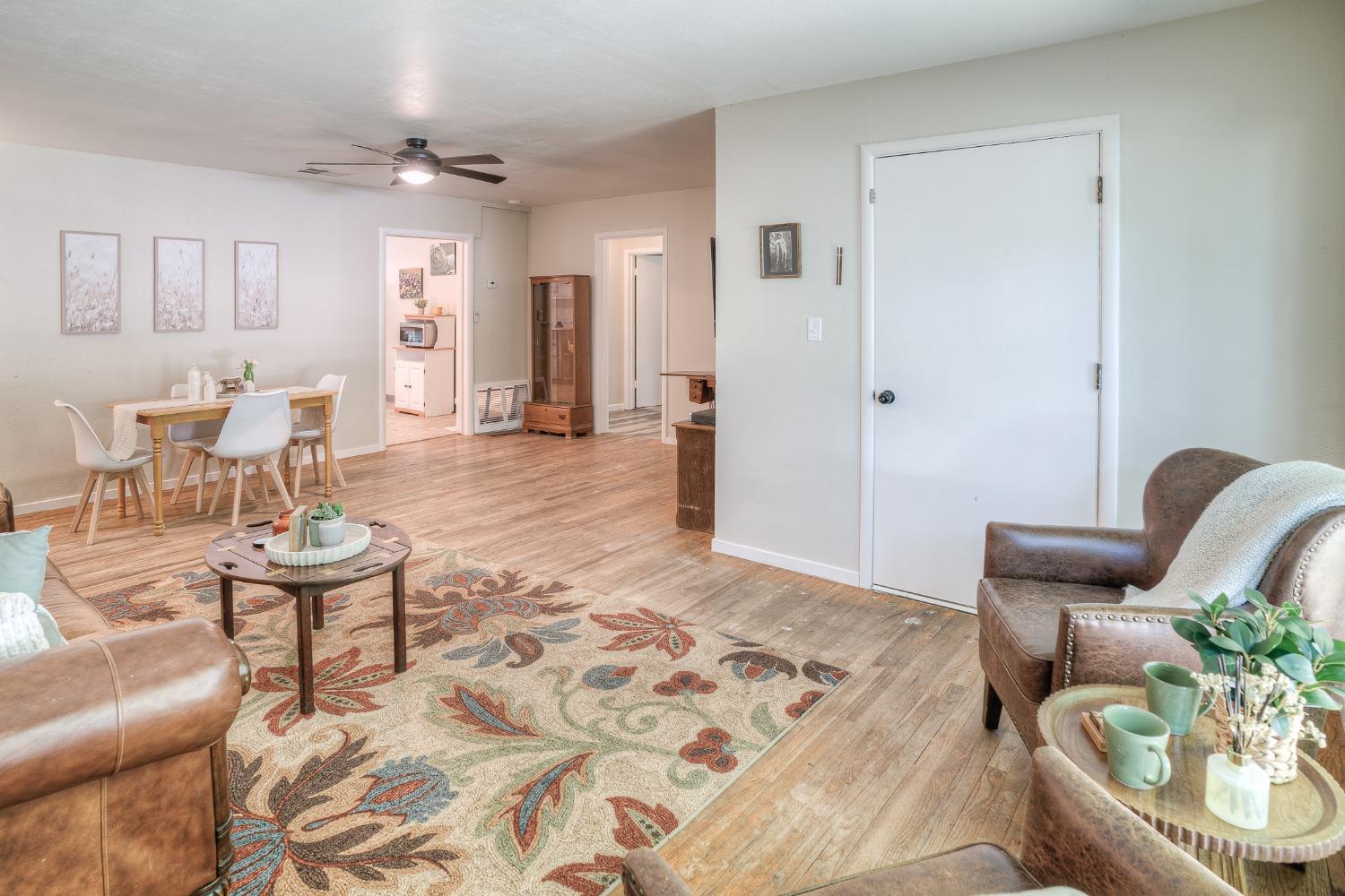 Open-plan living and dining room with a patterned rug, wood-look floors, and a ceiling fan.