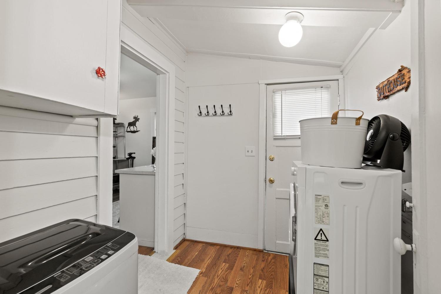 Laundry room with a washer and dryer, wood flooring, and a back door with blinds.