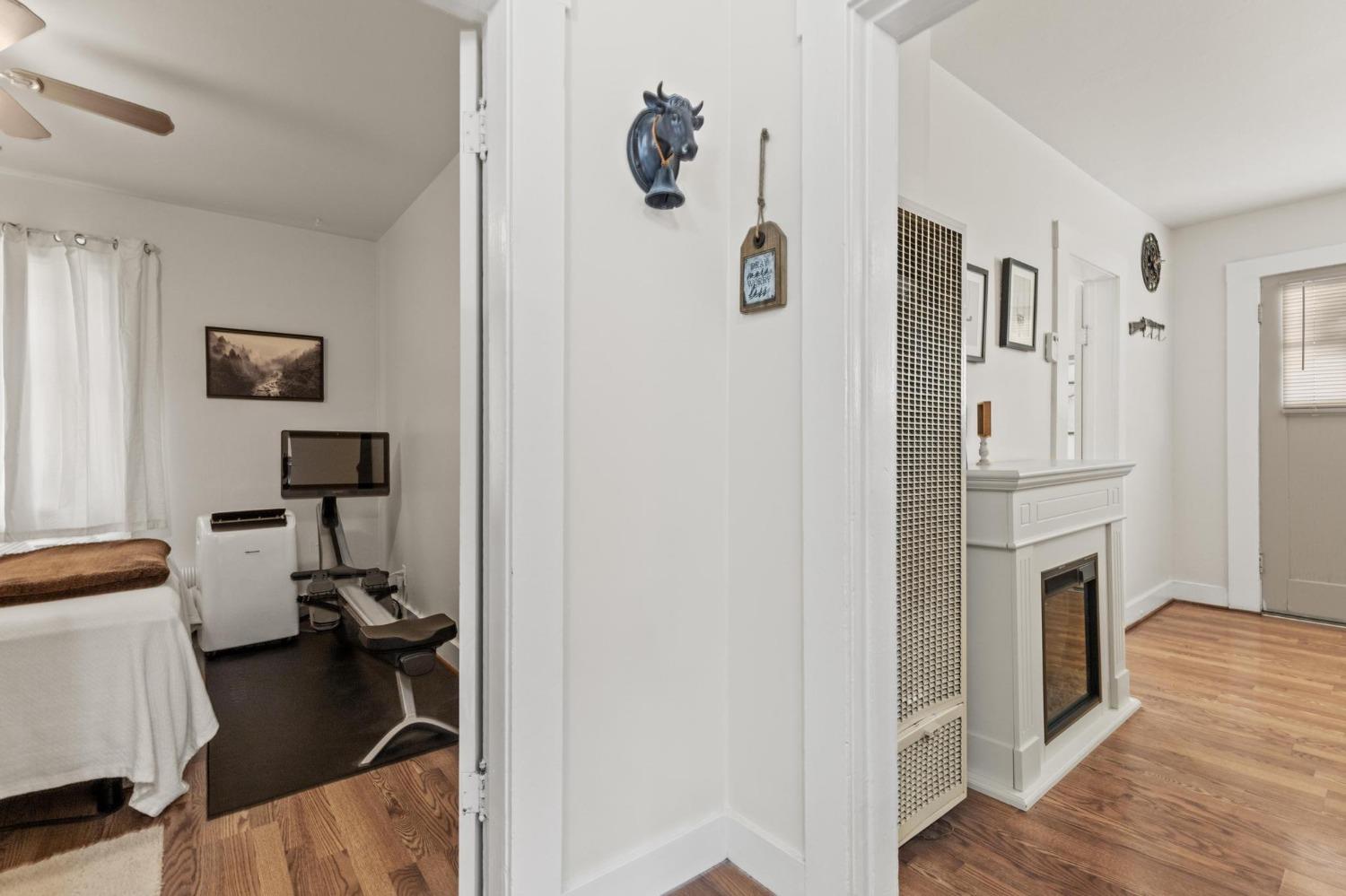 Home interior with a compact workout room beside a hallway fireplace and wood floors.