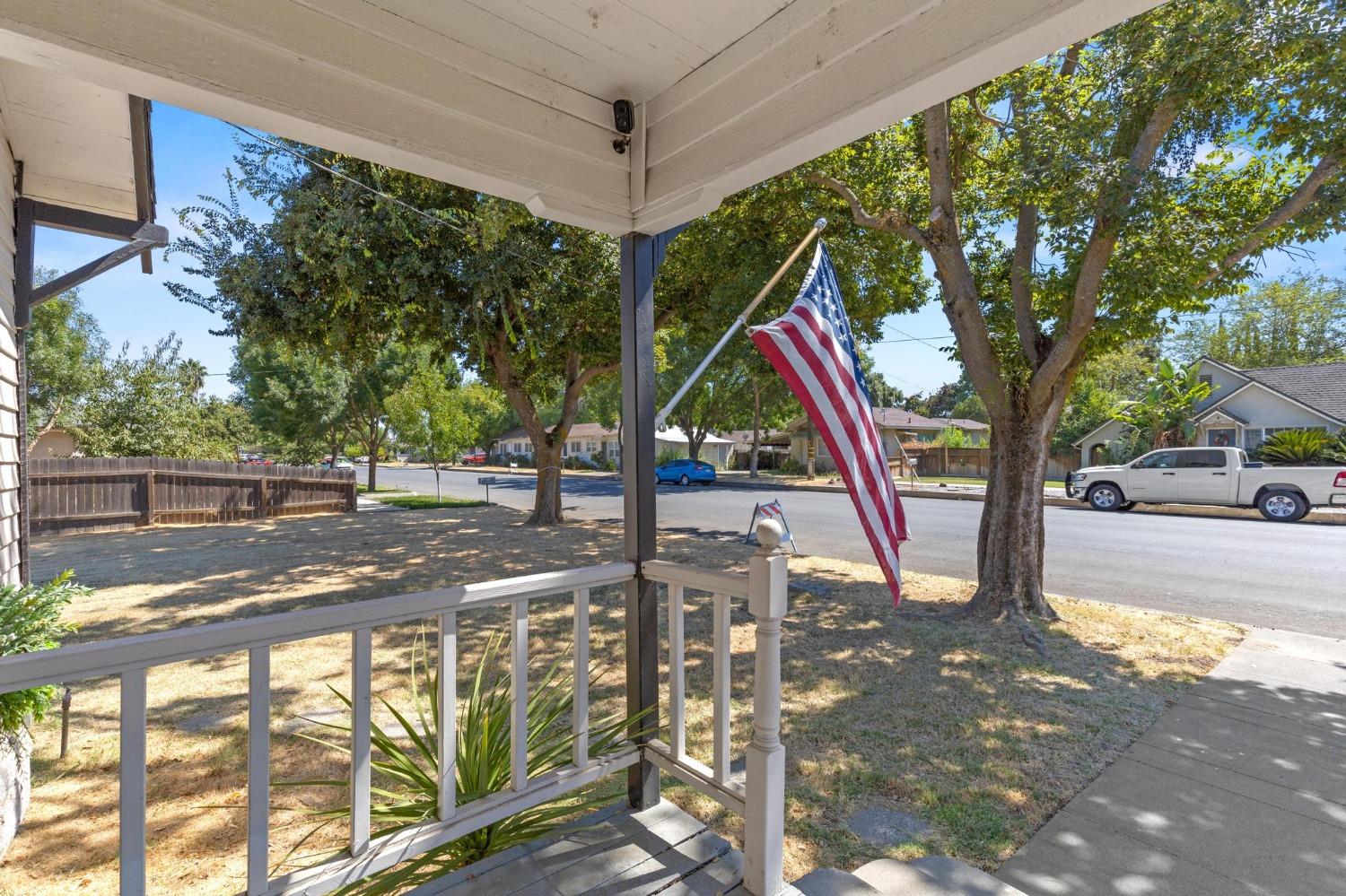 Covered front porch with an American flag overlooking a tree-lined residential street.