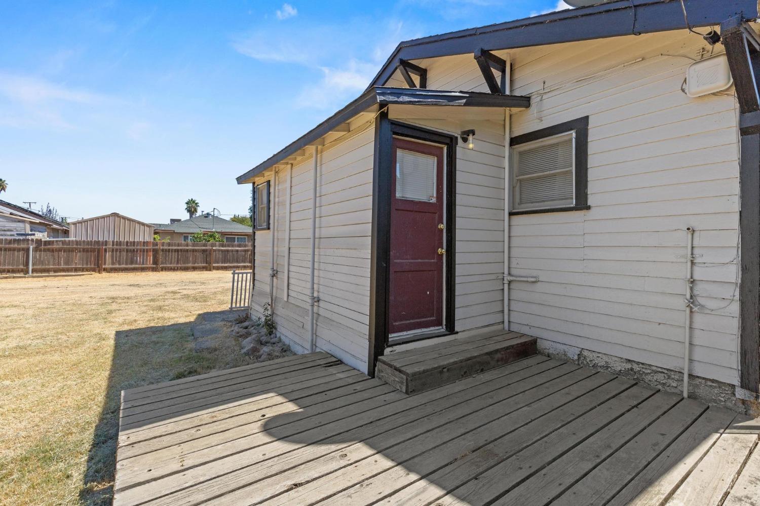 House exterior with a red door opening onto a broad wooden deck beside a fenced yard.