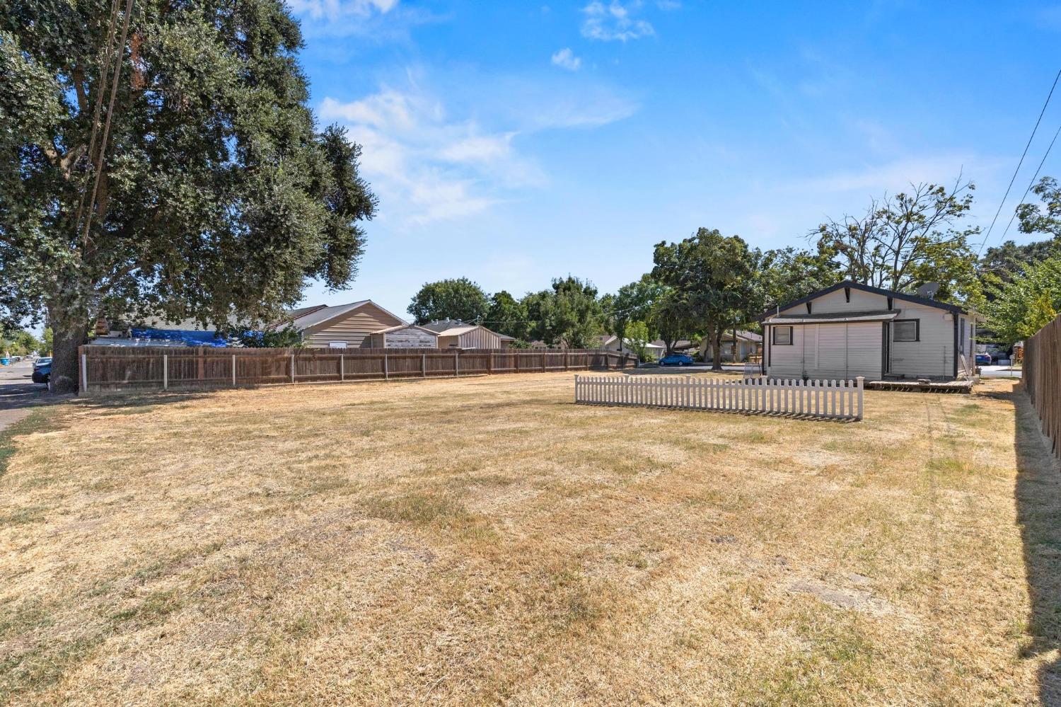Large fenced backyard with dry grass, a short white picket fence, and a small detached garage.
