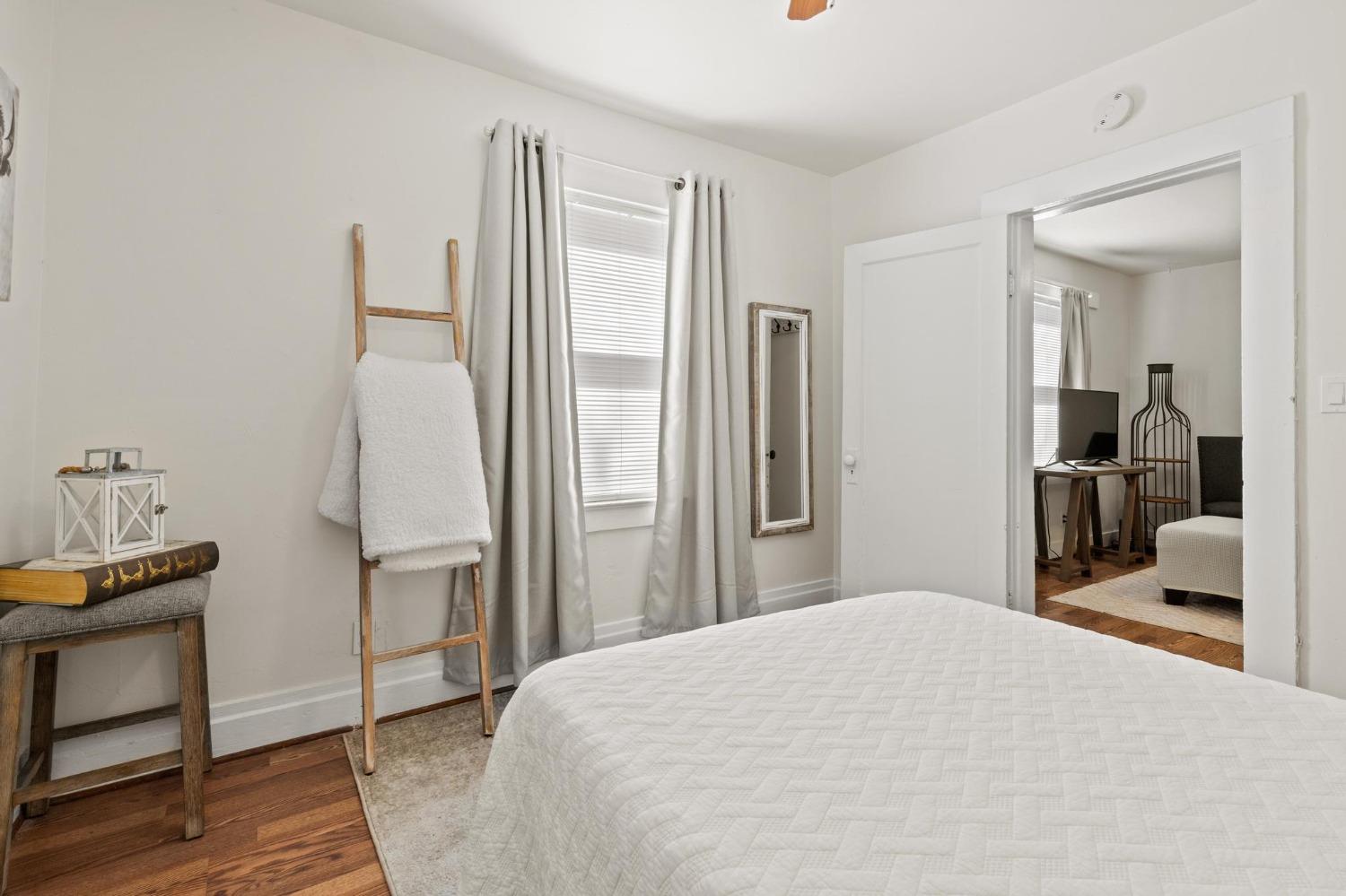 Staged bedroom with a white quilted bed, hardwood floors, and an open doorway to a sitting area.