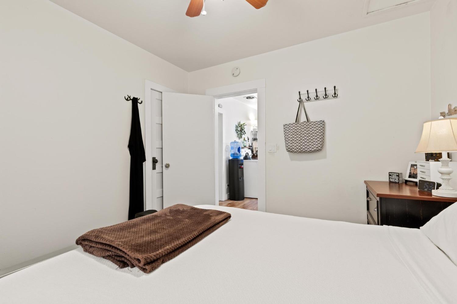 Bedroom with a white bed, folded brown blanket, and open door to an adjoining room.