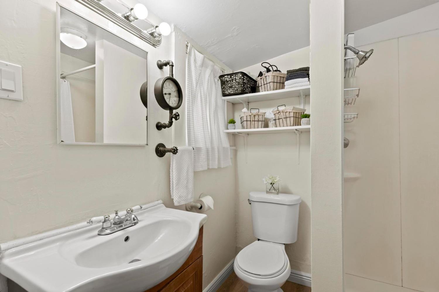 Bathroom with a white sink, wood vanity, toilet, and open shelves above the toilet.