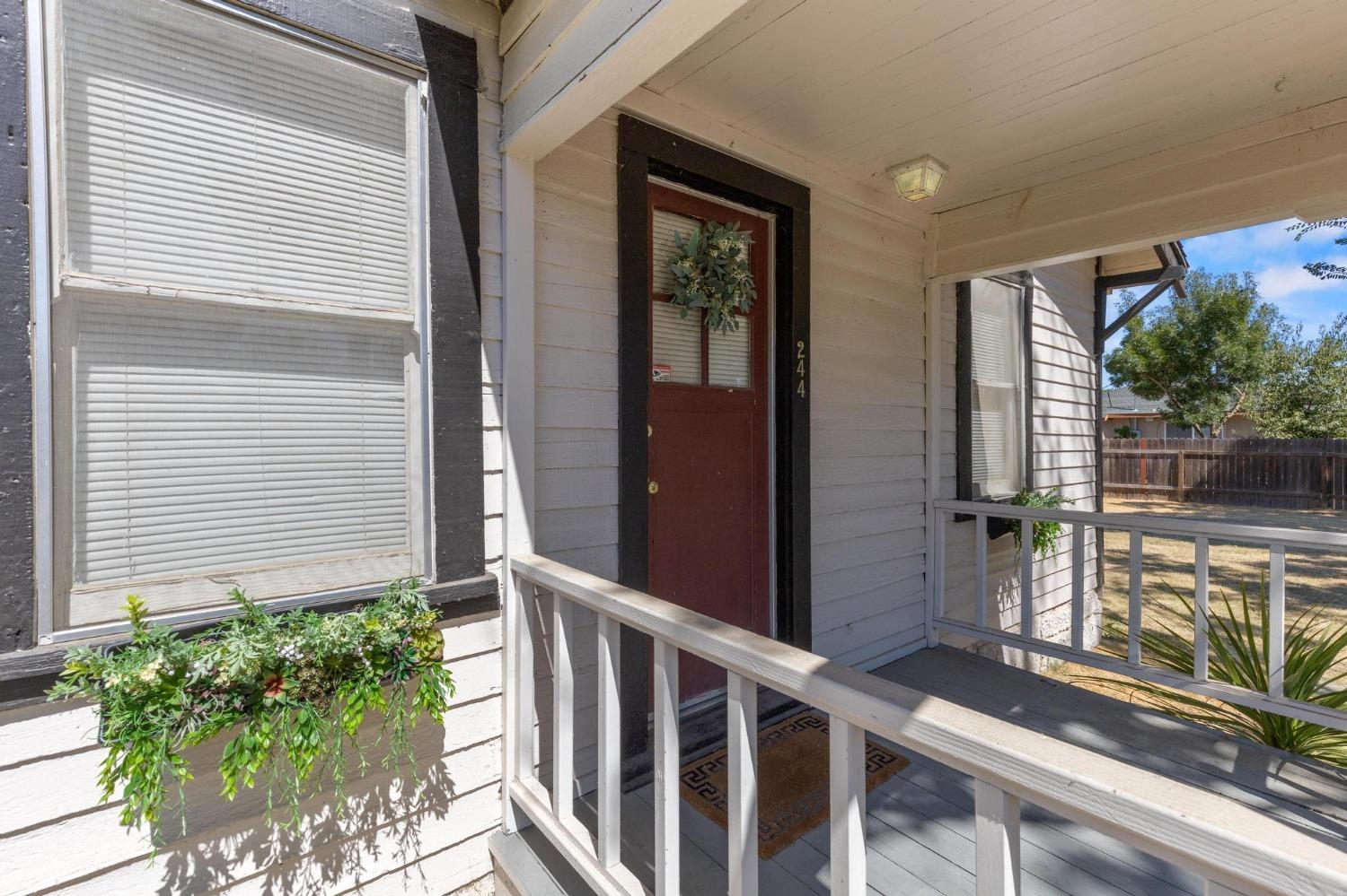 Covered front porch with a red entry door, leafy wreath, white railings, and potted greenery.