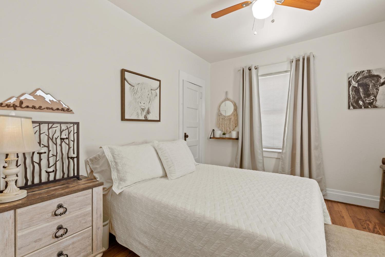 Furnished bedroom with a white quilted bed, hardwood floors, and animal artwork.