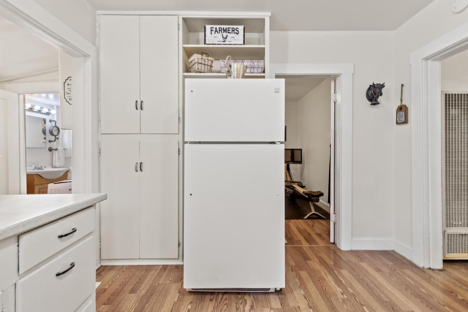 Kitchen with white cabinets and refrigerator, hardwood floors, and doorways to a bathroom and office.