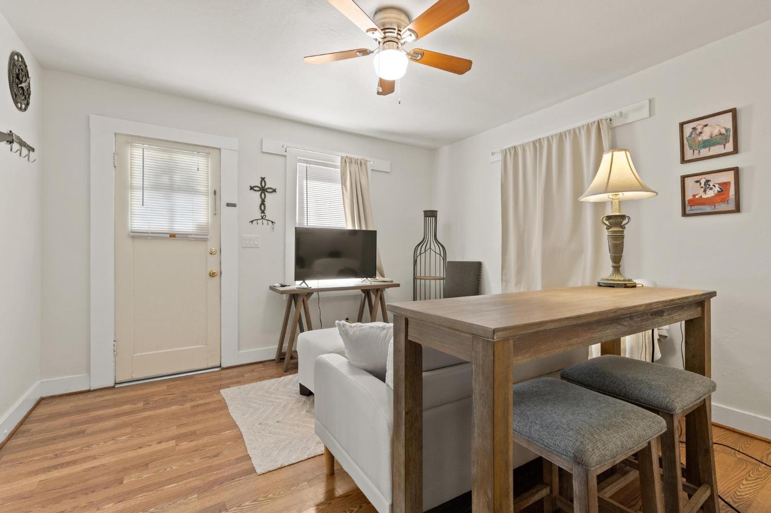 Living and dining area with hardwood floors, a wooden table, white sofa, and television by the front door.