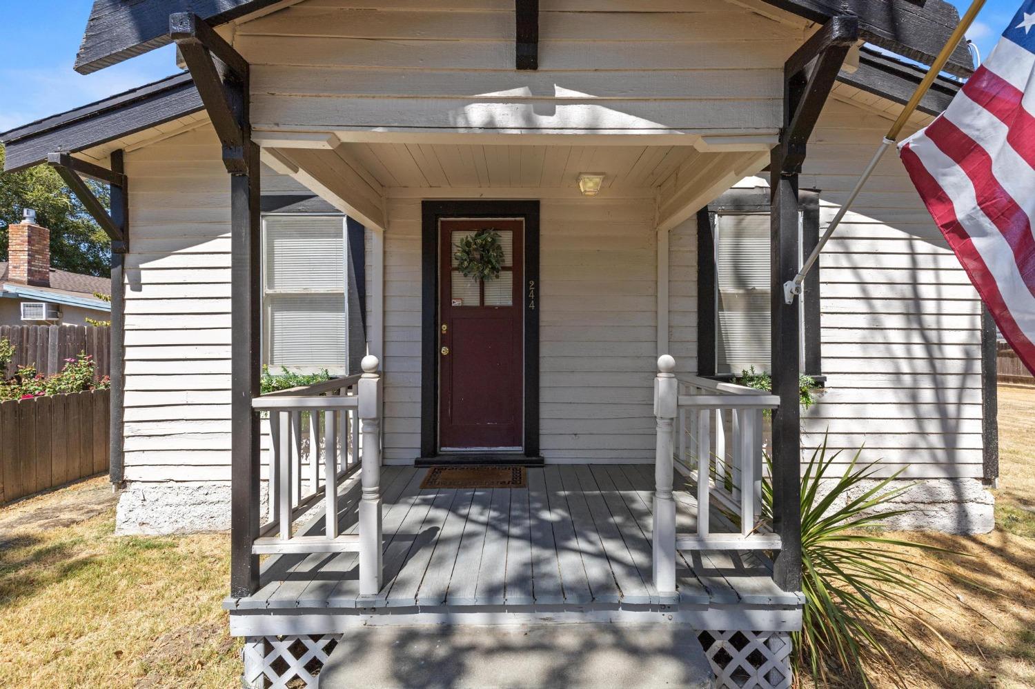 House entrance with a covered porch, white railings, burgundy door, and American flag.