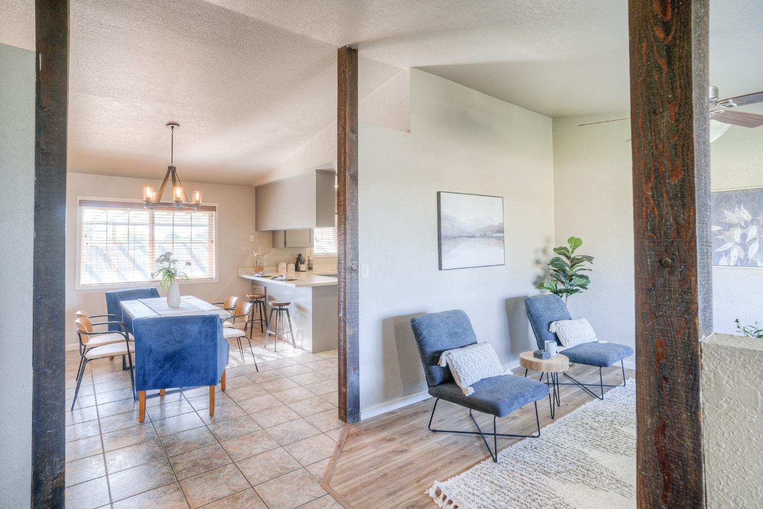 Open-plan living and dining area with blue chairs, a tiled dining space, and dark wood posts.