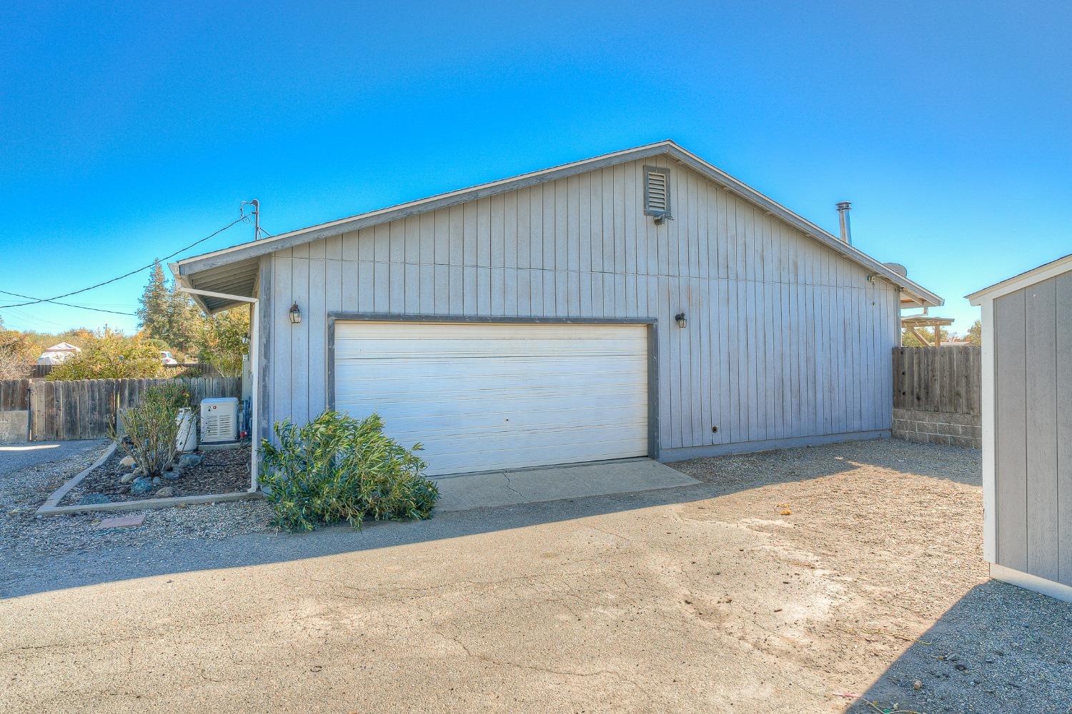 Detached gray garage with a wide white door and concrete driveway.