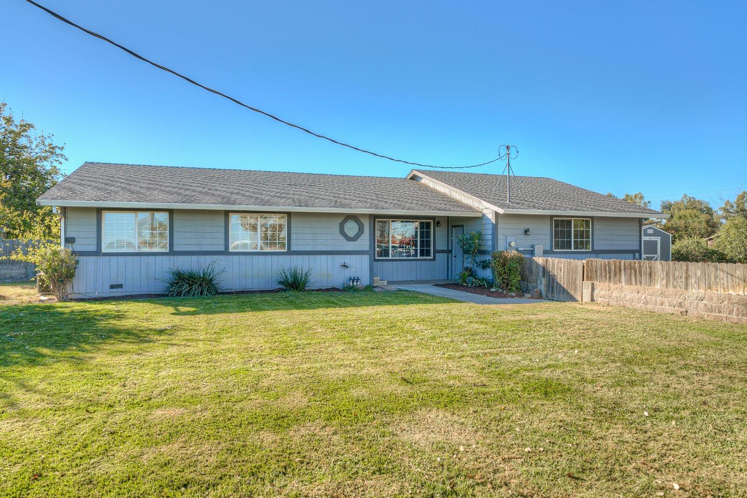 Single-story blue-gray ranch house with a broad front lawn and wooden fence.