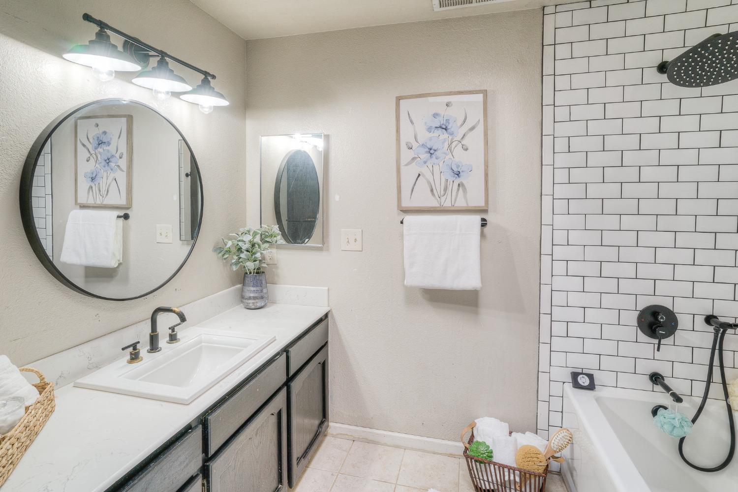 Bathroom with a white vanity, round mirror, and subway-tiled bathtub.