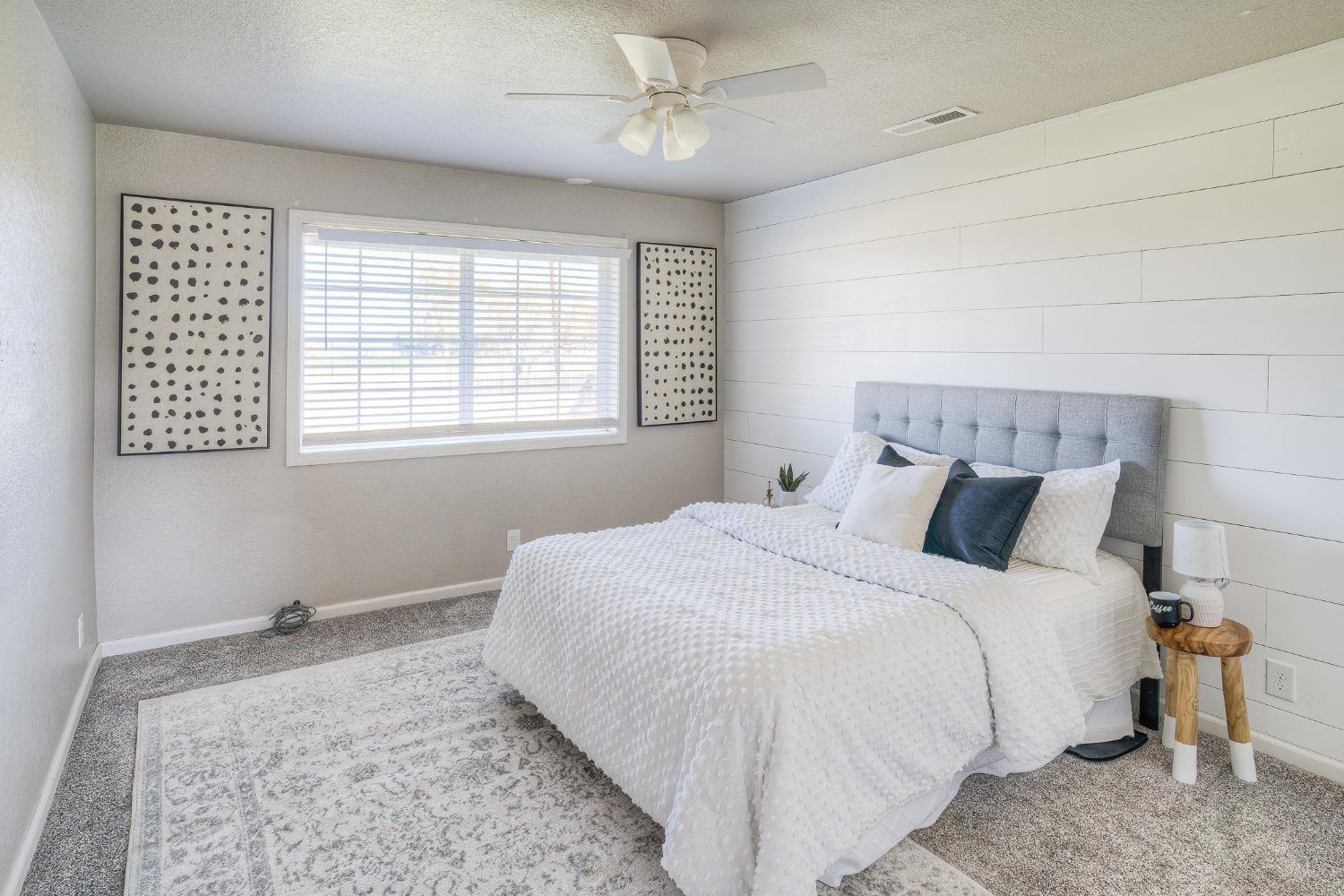 Staged bedroom with a white bed, gray upholstered headboard, and white shiplap accent wall.